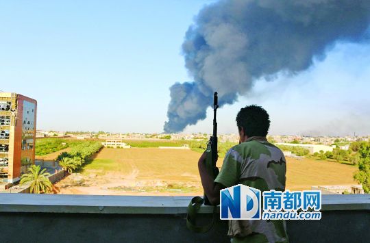 2日，利比亞首都的黎波里，一民兵武裝成員眺望被火箭彈擊中的儲油罐冒出濃煙。